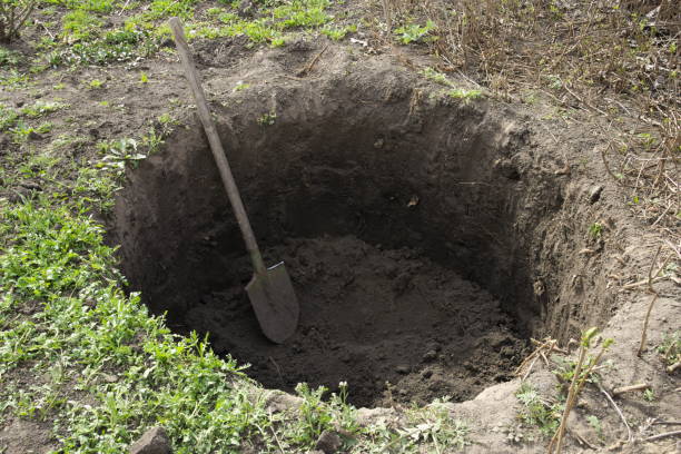 Deep pit in the ground. In the pit lies a shovel. Digging a hole.